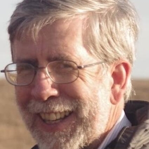 A man with glasses and gray hair and beard smiles at the camera